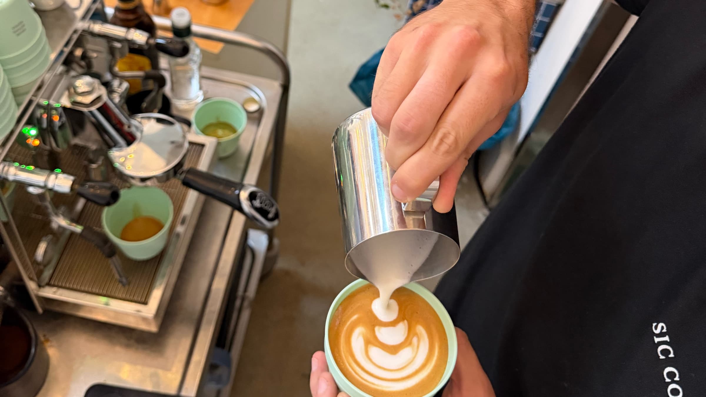 Barista gießt Latte Art in einen Becher neben der Siebträgermaschine der mobilen Kaffeebar