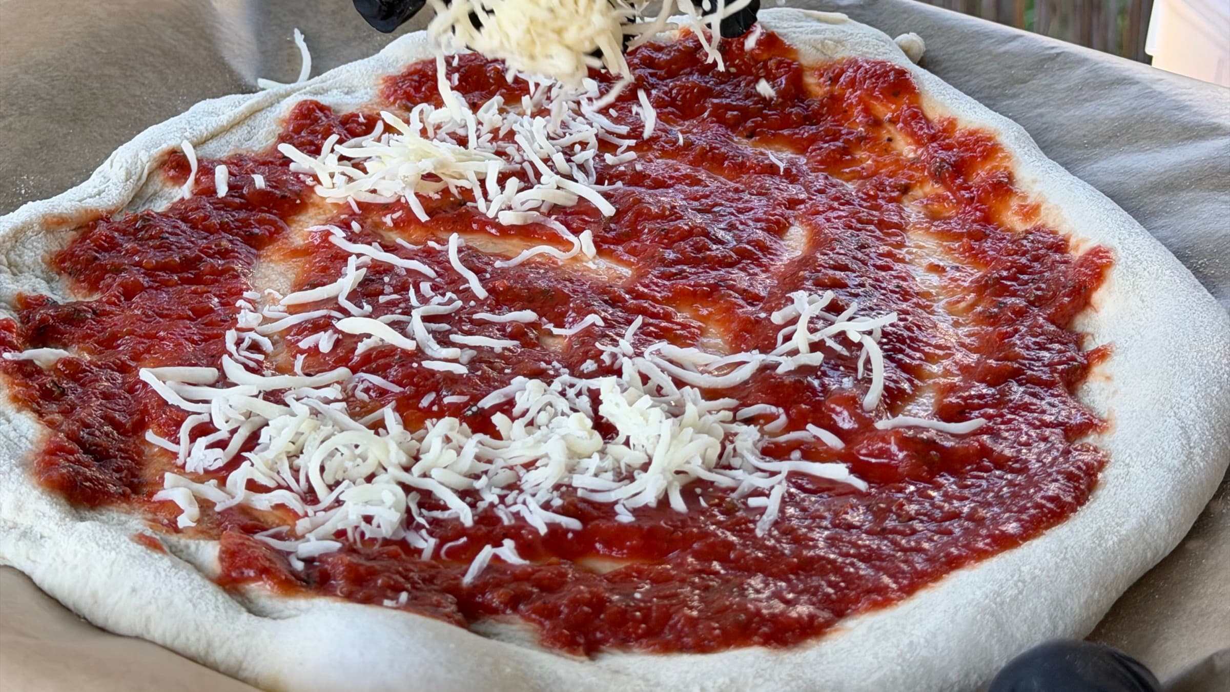 Pizza wird im Garten vor einem Bambuszaun mit Käse belegt