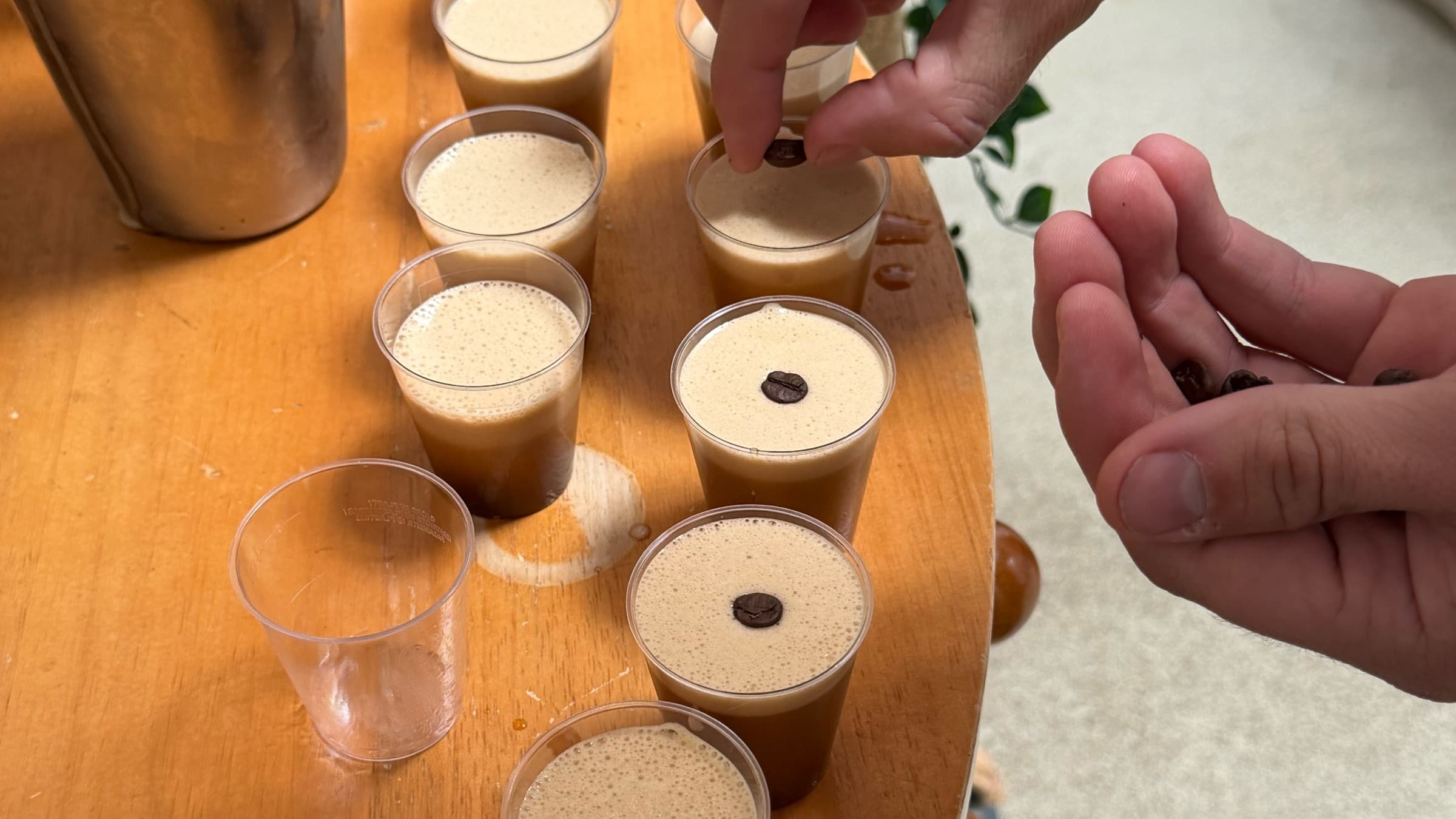Reihe kleiner Becher mit Espresso, obenauf wird je eine Kaffeebohne gelegt