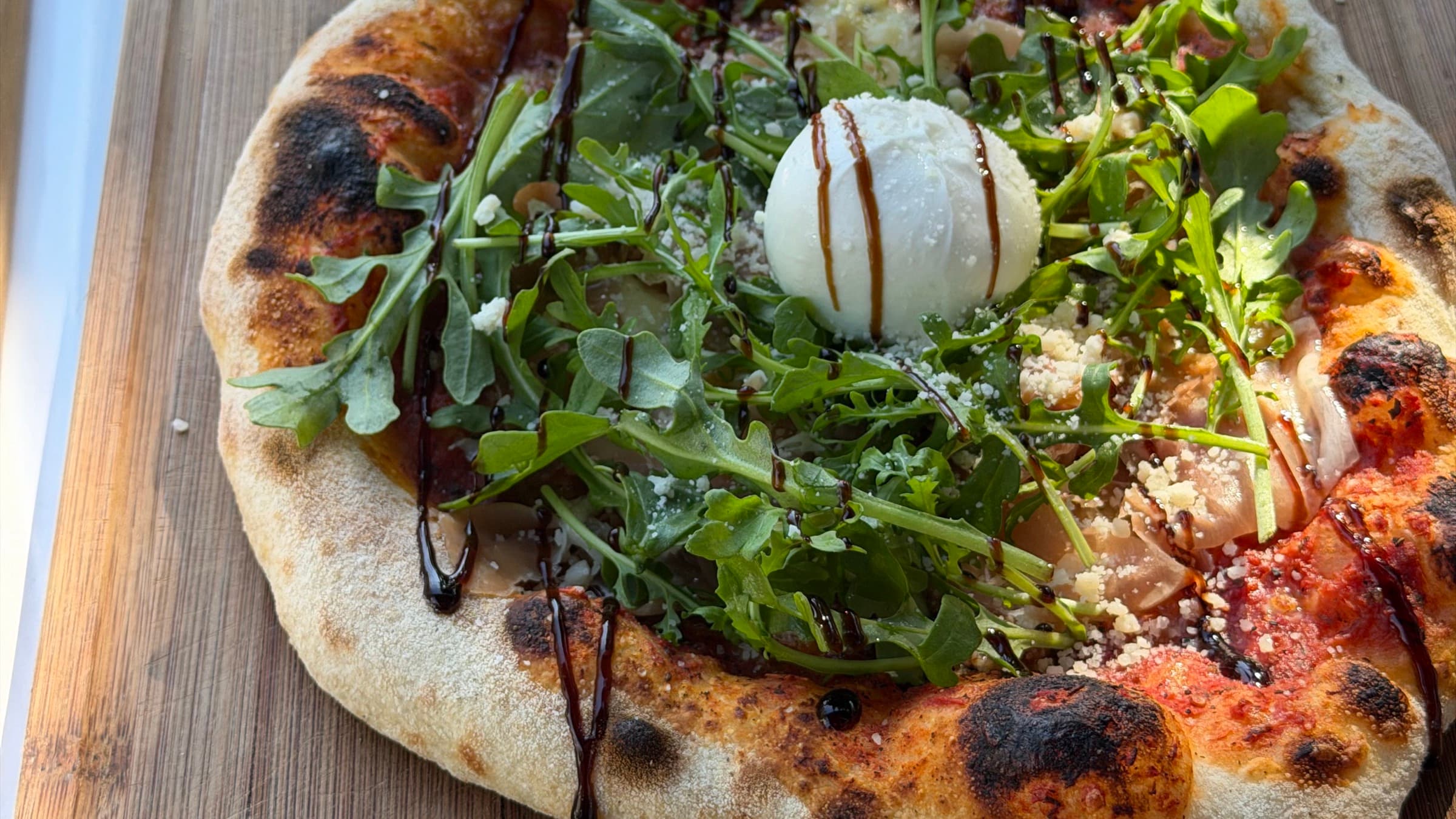 Pizza mit Rucola und Burrata wird mit Balsamico verfeinert