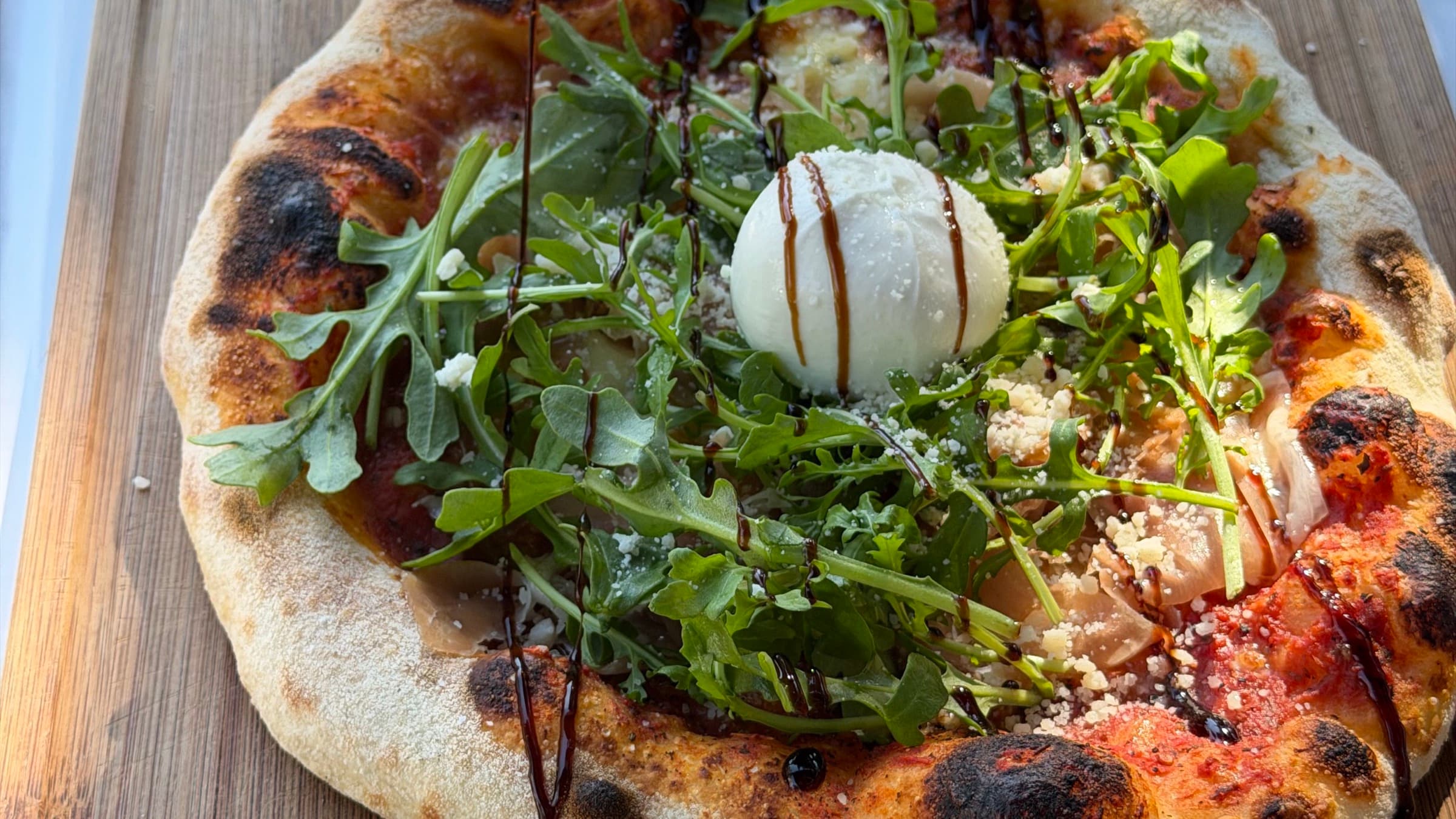 Pizza mit Burrata, Rucola und Balsamico auf einem Holzbrett